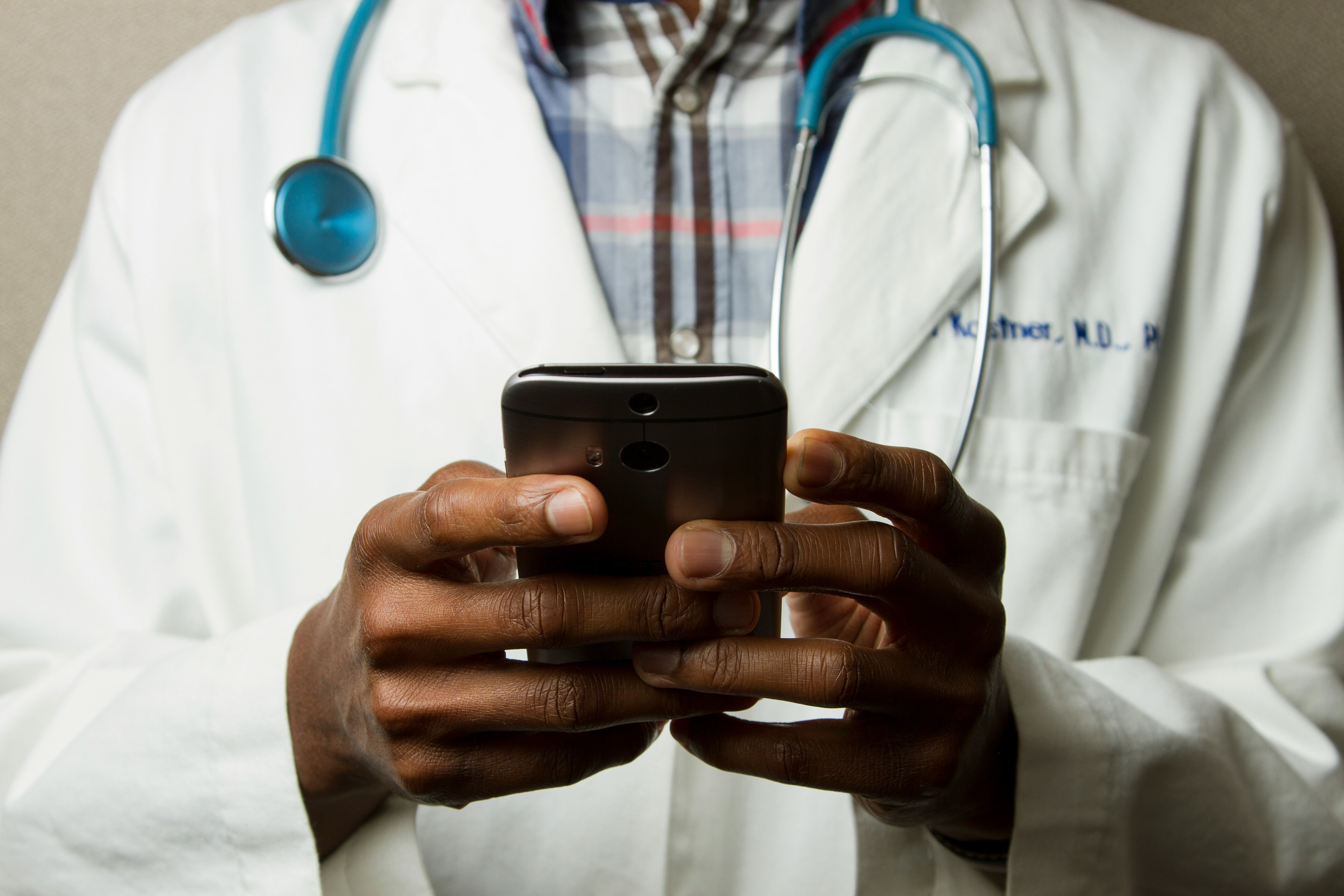 An image of a doctor holding a phone with a stethoscope in their neck
